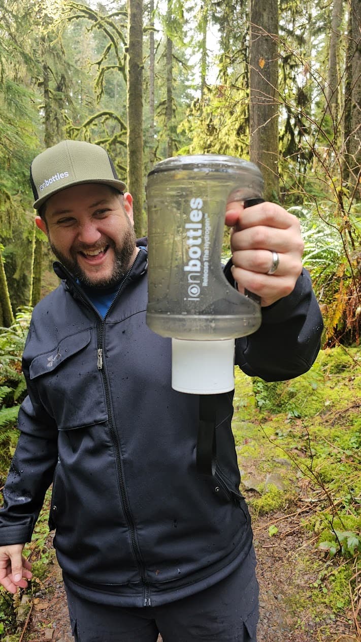 Bobby Samai, founder of ionbottles and EcomDads, in the woods holding an ionbottles jug